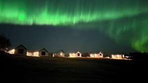 Une rangée de petites maisons, toutes conçues dans le même style, offrant une vue dégagée sur le ciel nocturne et les aurores boréales.