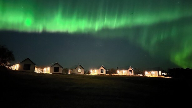 A row of small, uniformly designed houses with a clear view of the night sky and the Northern Lights.