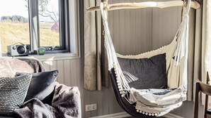 Une pièce chaleureuse avec un fauteuil suspendu en forme de hamac, une fenêtre donnant sur un champ et une radio posée sur le rebord de la fenêtre.
