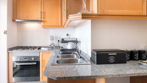 A kitchen with wooden cabinets, a stainless steel sink, a built-in oven, and a bread box.