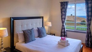 A neatly made bed with pillows, a bedside lamp, and a window with curtains.