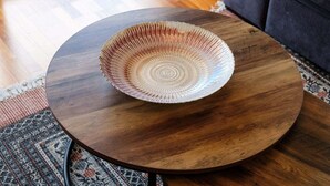 A round wooden table with a decorative bowl on it, placed on a patterned rug.