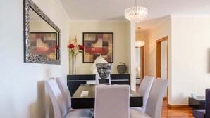 A dining area with a black table, white chairs, and a red rug. There are two framed artworks on the wall and a chandelier above the table.