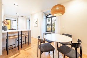 A modern kitchen with a dining area, featuring a round table, dark chairs, and a woven pendant light. - GuestReady - Conde das Acáçovas 1E (Oeiras)