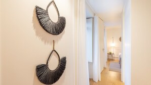 Corredor com duas peças decorativas fixadas na parede e uma visão de quarto com cama e mesa de cabeceira.