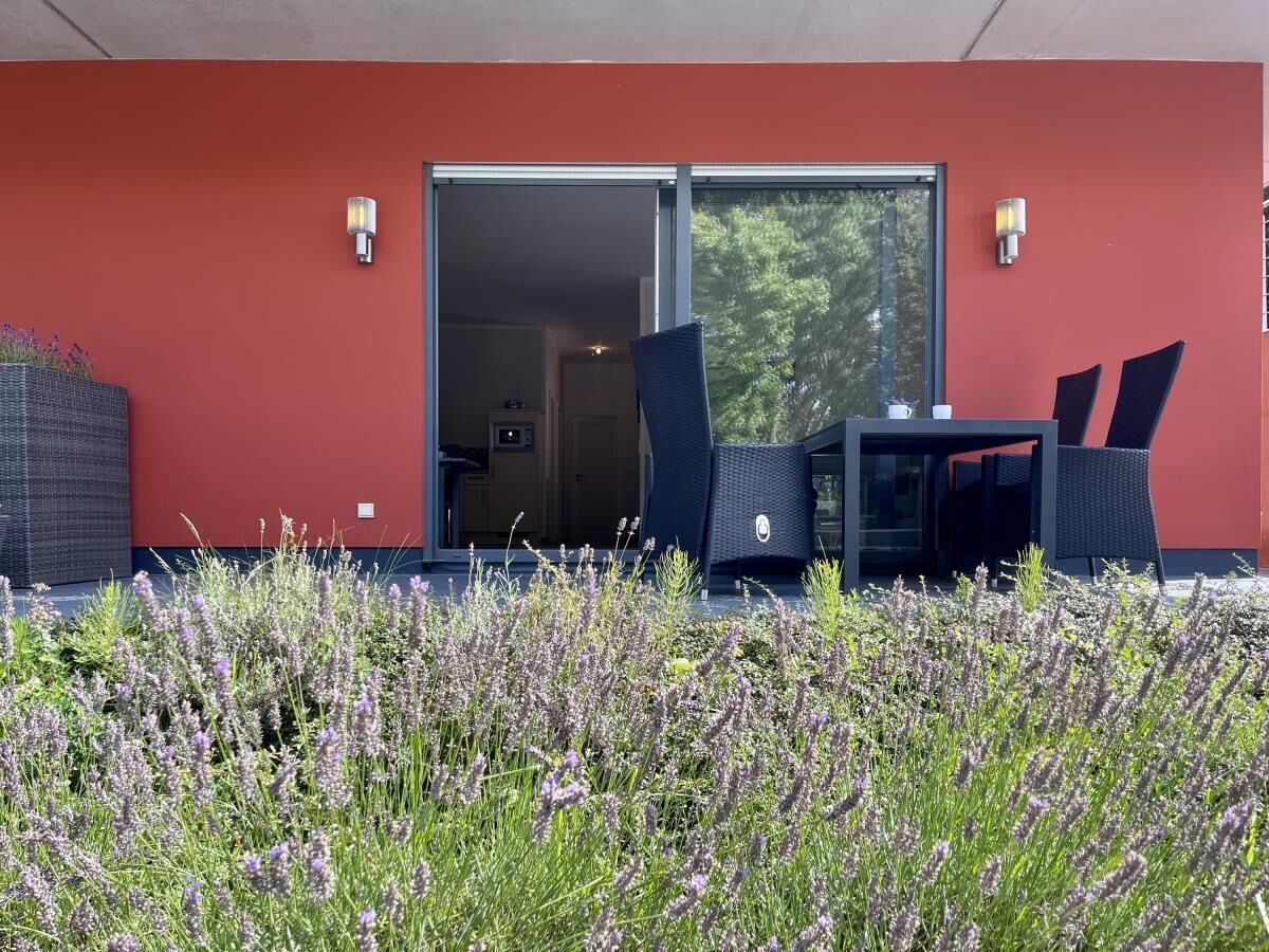 A modern outdoor seating area with a red wall, two chairs, and a table.
