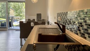 A modern kitchen with a large island, a glass backsplash, and a dining area with chairs and a table. - Amselresidenz 1 - AMSEL (Binz)