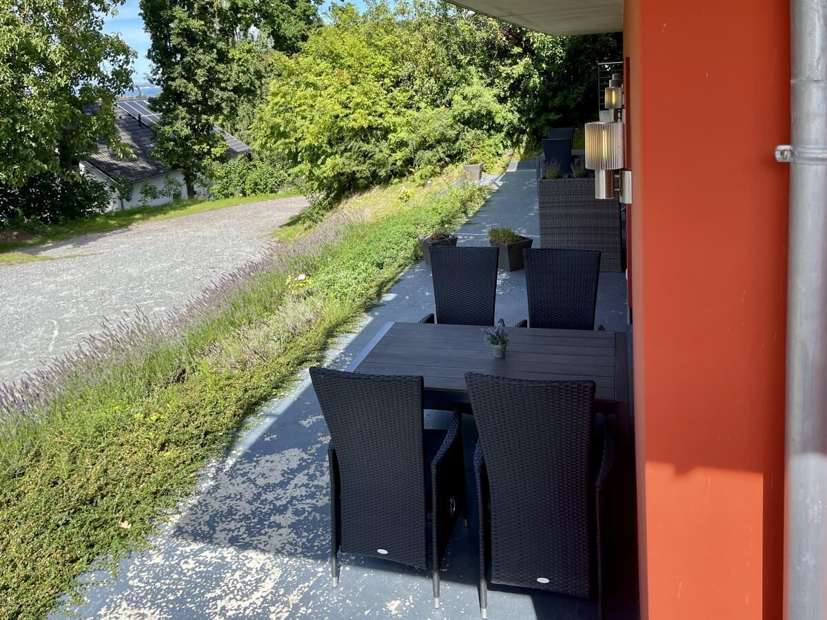 An outdoor seating area with wicker tables and chairs, a gravel path, and greenery in the background.