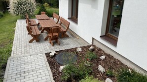 A patio with a wooden table and benches, surrounded by a garden with various plants and a small tree. - Residence Dymokury (Stredoceský kraj)