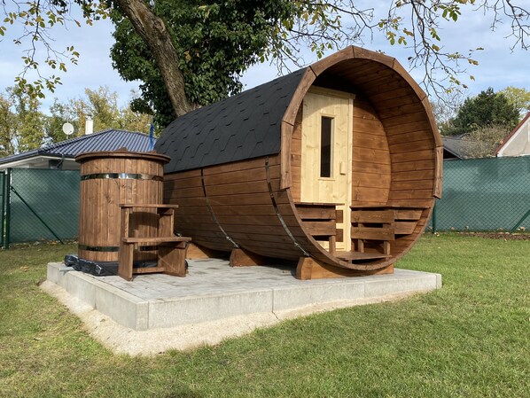 Una estructura de madera con forma de barril, una puerta, un banco de madera pequeño y un objeto cilíndrico con una escalera.