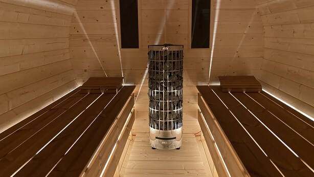 A sauna room with wooden benches and a central stone heater. - Residence Dymokury (Stredoceský kraj)