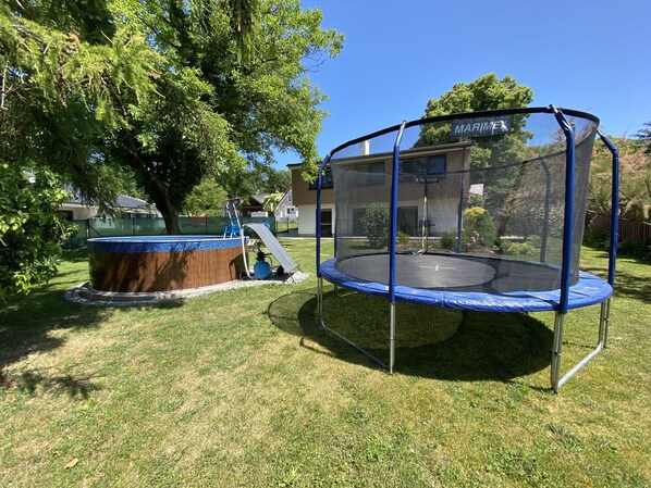 A backyard with a trampoline, a hot tub, and a tree.