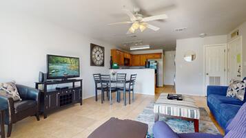 A living room with a TV, a dining table with chairs, a sofa, a coffee table, and a ceiling fan.
