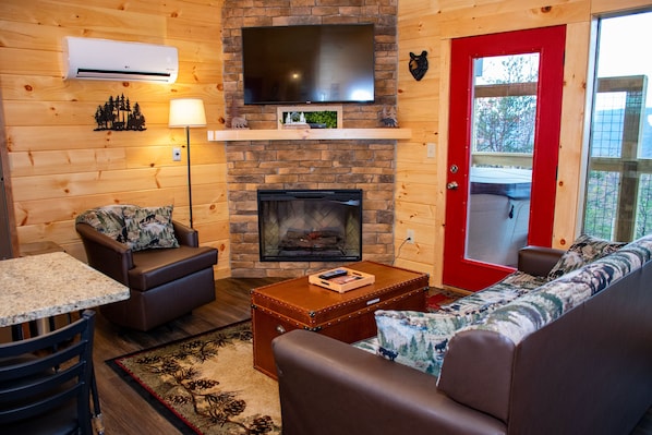 A cozy living room with a fireplace, leather furniture, a flat-screen TV, and a red door. - COMFY COTTAGE II - Built in 2023 with Amazing Valley Views! (Sevierville)