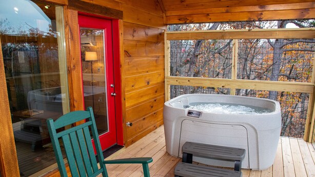 Eine Holzterrasse mit einem Whirlpool, einer roten Tür und einem grünen Stuhl.