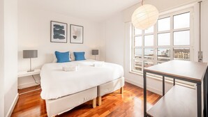 Ein modernes Schlafzimmer mit einem großen Bett, einem Schreibtisch und Blick auf die Stadt durch große Fenster.