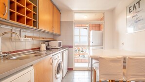 Eine kompakte Küche mit Spüle, Mikrowelle und Waschmaschine. Ein Essbereich mit Tisch und Stühlen ist ebenfalls vorhanden.