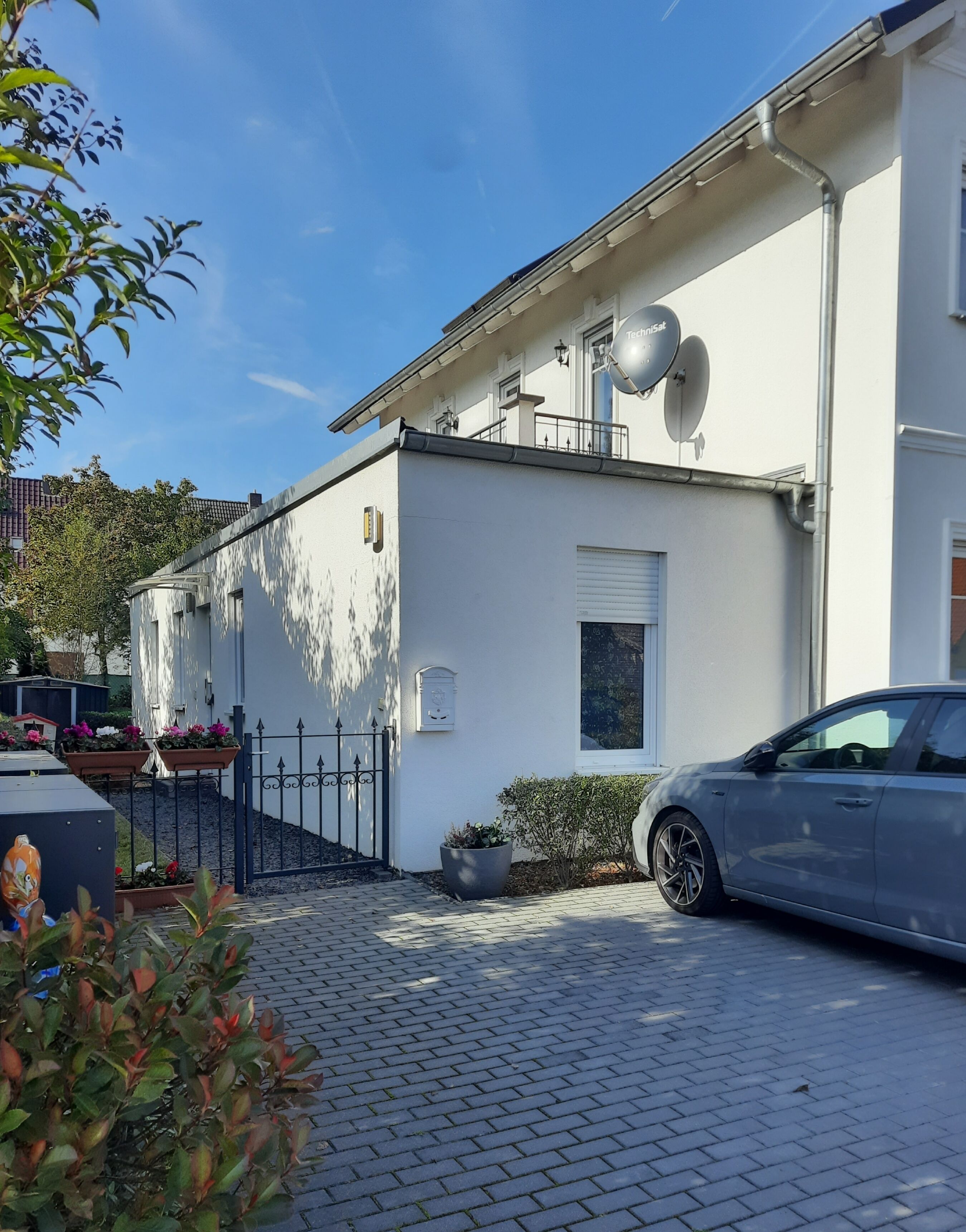 En modern vit byggnad med satellitantenner, en bil parkerad framför och en asfalterad uppfart.