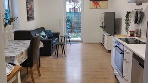 A modern kitchen with a built-in oven and microwave, a dining area with a table and chairs, and a living room with a sofa and a TV. - Moderne WHG in Churfranken: Fahrrad-wandertouren & Geschäftlich/monteuer😊 (Elsenfeld)