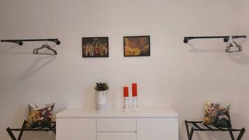 Een wit bureau met twee rode kaarsen, een vaas met groene planten en twee schilderijen aan de muur.