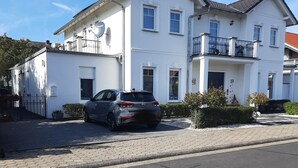 A two-story white building with a balcony, a car parked in front, and a satellite dish on the roof. - Moderne WHG in Churfranken: Fahrrad-wandertouren & Geschäftlich/monteuer😊 (Elsenfeld)