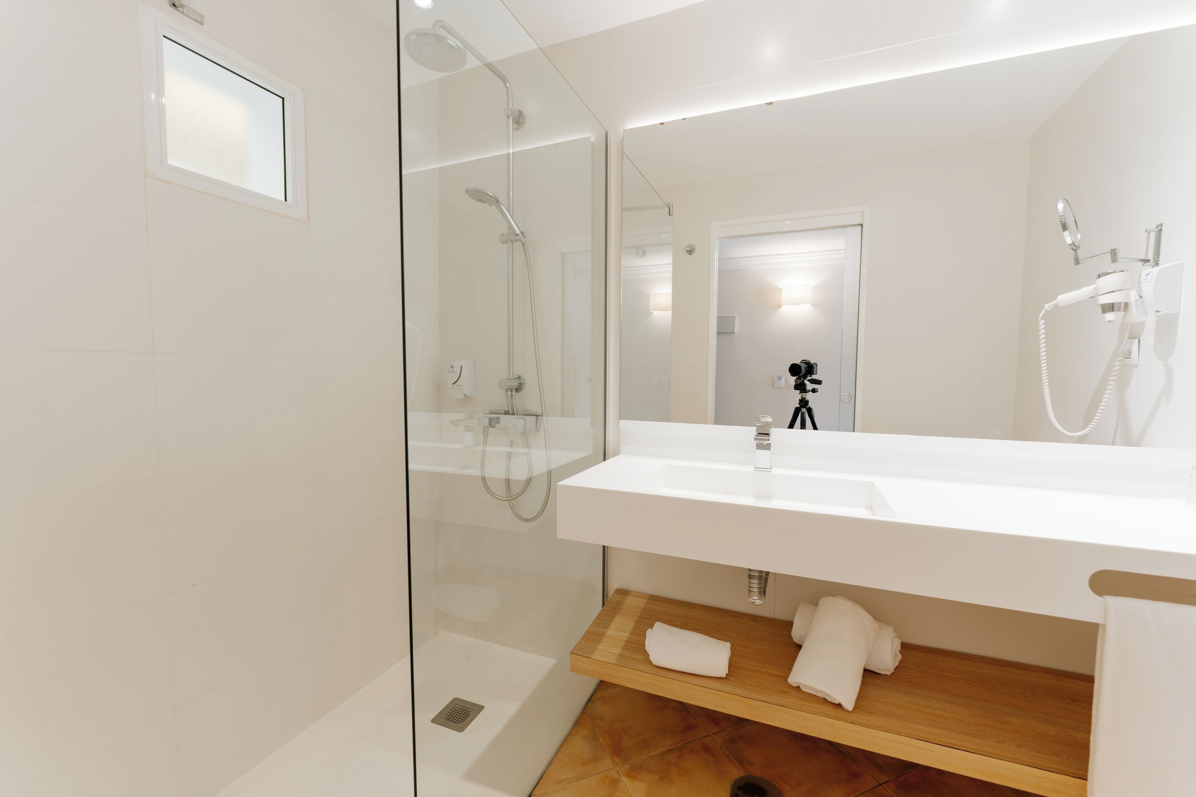 Une salle de bain moderne avec une douche à parois de verre, un lavabo blanc et une étagère en bois où sont posées des serviettes.