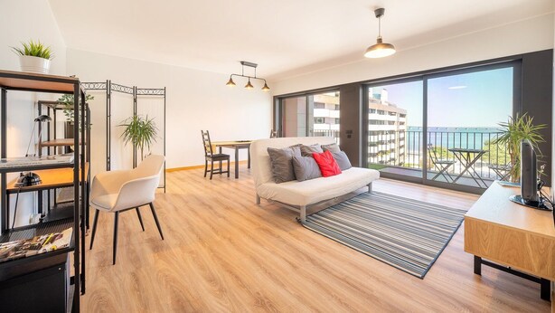 Ein modernes Wohnzimmer mit einer Couch, einem Esstisch und Stühlen. Ein Balkon bietet Blick auf das Meer.