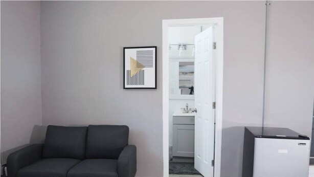 A modern living room with a dark sofa, a small round table, and a refrigerator. - Whimsical 2BR 10-Mins to Nashville (Nashville)