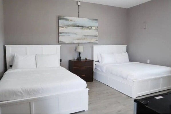 A bedroom with two white beds, a nightstand with a lamp, and a painting on the wall.