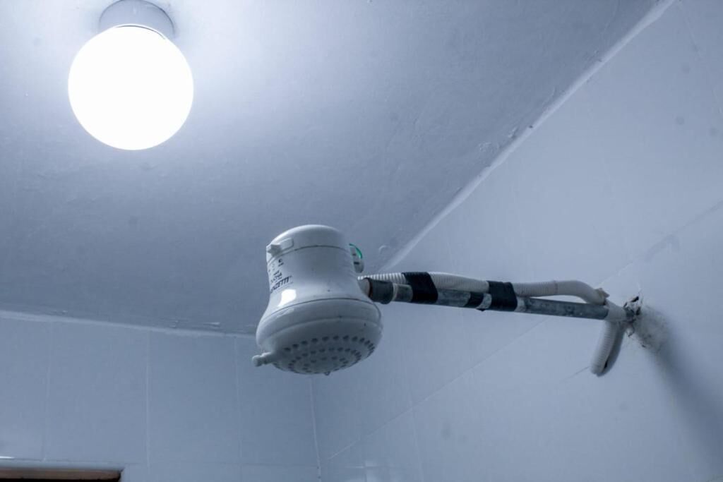 Un cabezal de ducha instalado en el techo con manguera, un accesorio de iluminación y un tubo visible.