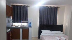 Een compacte kamer met een bed, een kleine kitchenette en een raam met gordijnen.