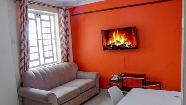 Een woonkamer met een bank, een tv aan een oranje muur, een kleine tafel en een raam met gordijnen.