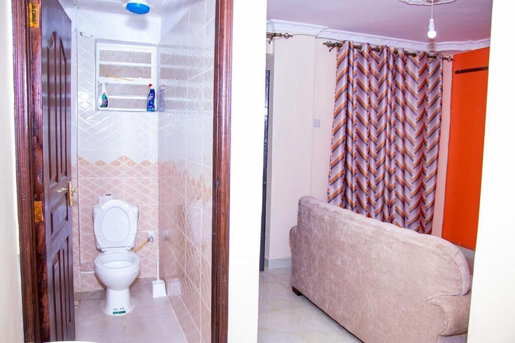 A bathroom with a toilet, a shelf with cleaning supplies, and a shower curtain.