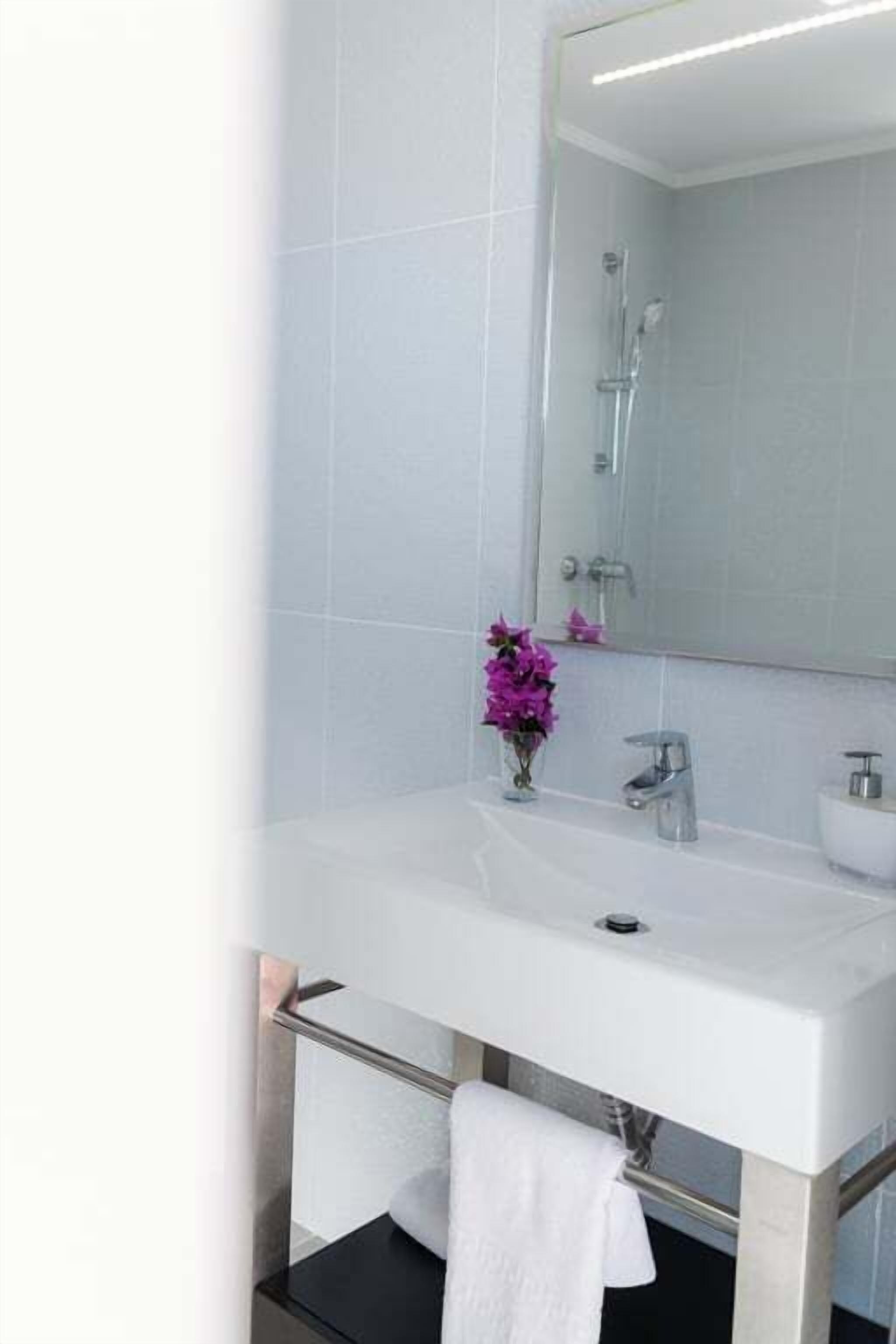 Ein modernes Badezimmer mit einem weißen Waschbecken, einem Spiegel und einer Dusche.