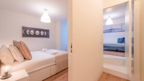 A bedroom with a bed, pillows, a bedside table, a lamp, and a wall-mounted picture of moon phases. - GuestReady - Pink Sunset (Lisbon)