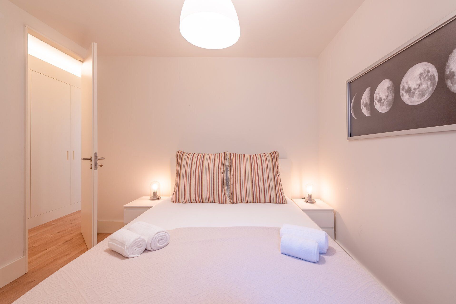 Ein Schlafzimmer mit einem Bett, zwei Nachttischen, einer Tür, einem Wandbild mit Monden und einer Lampenleuchte.