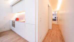 A modern kitchen with white cabinetry, a built-in oven, and a red towel hanging on the countertop. - GuestReady - Pink Sunset (Lisbon)