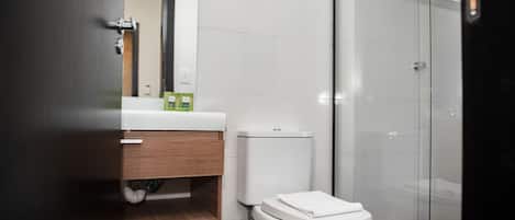 Un baño moderno con inodoro, lavamanos con espejo y zona de ducha.