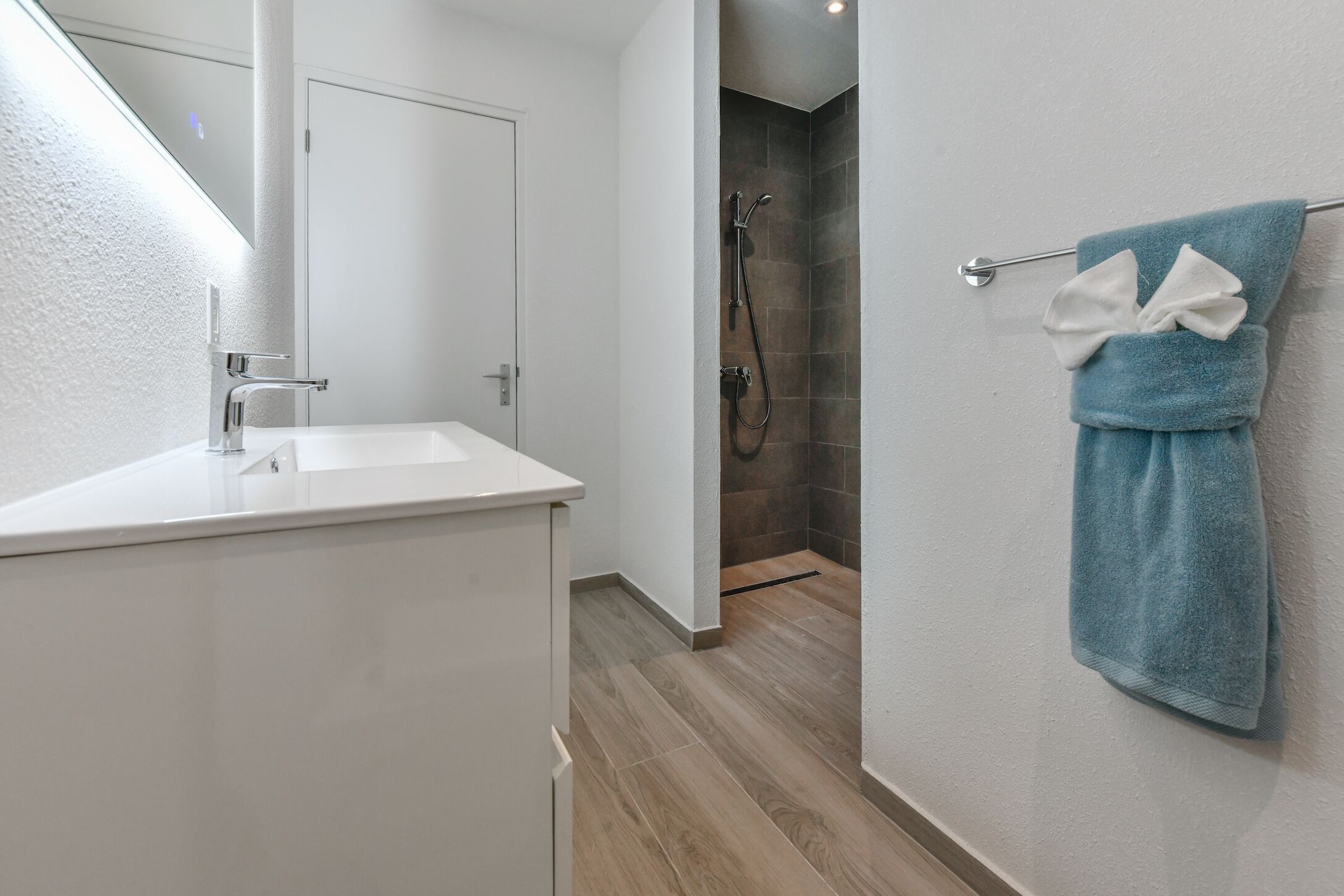 Een moderne badkamer met een witte wastafel, een douche en een handdoekrek met een blauwe handdoek.