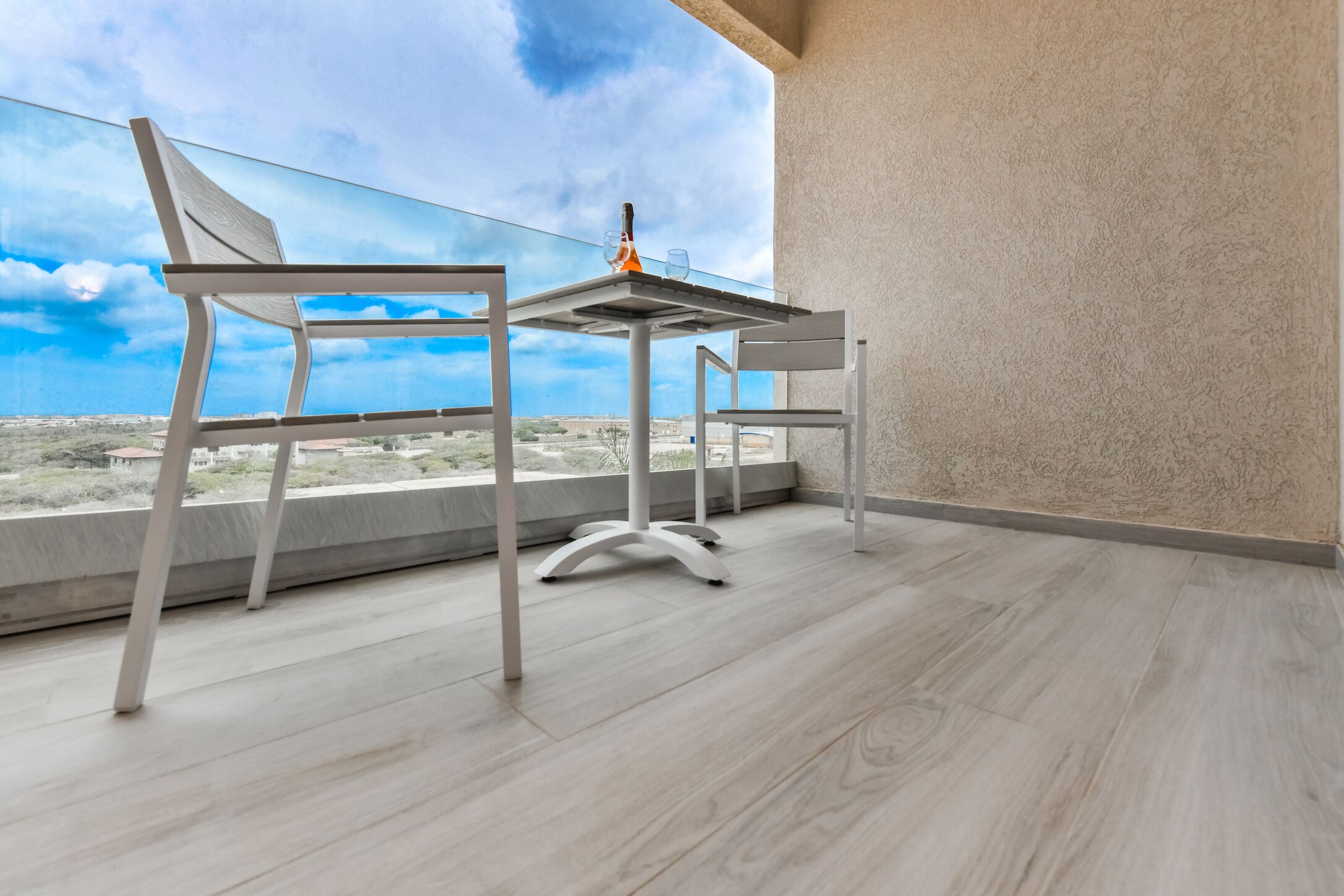 Un balcon avec une table et des chaises, une bouteille et des verres.