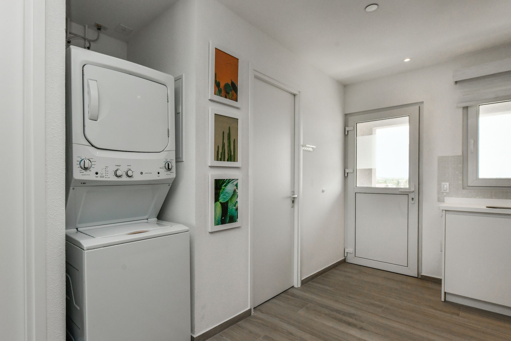 A laundry area with a washer and dryer, a door with a window, and a small cabinet.