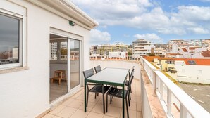 A balcony with a table and chairs, a sliding glass door, and a view of a residential area with buildings. - GuestReady - Sunny Retreat in Costa da Caparica (Costa da Caparica)