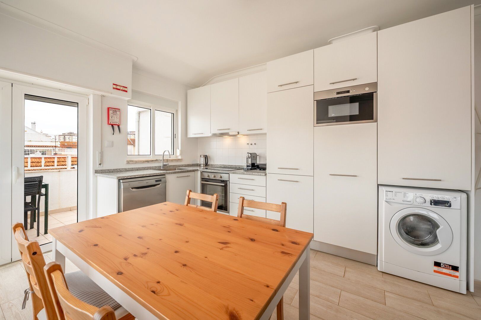 Une cuisine moderne avec des meubles blancs, une table à manger en bois et un lave-linge encastré.