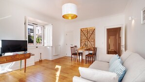 A modern living room with a flat-screen TV, wooden furniture, and a dining area with a table and chairs. - GuestReady - Sunny Chic in Santos (Lisbon)