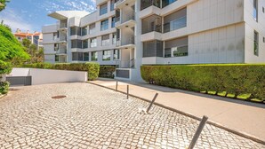 Un moderno edificio residenziale a più piani con balconi, un cortile lastricato e siepi curate.