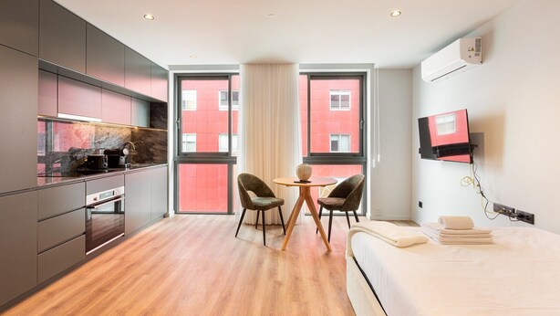 A modern hotel room with a kitchen, dining area, and a bed.