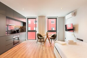 A modern hotel room with a kitchen, dining area, and a bed.
