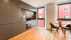 A modern kitchen with dark cabinetry, a built-in oven, and a dining area with a round table and two chairs.