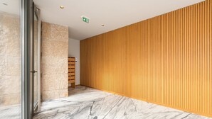 A hallway with a marble floor, a wooden panel wall, and a glass door.