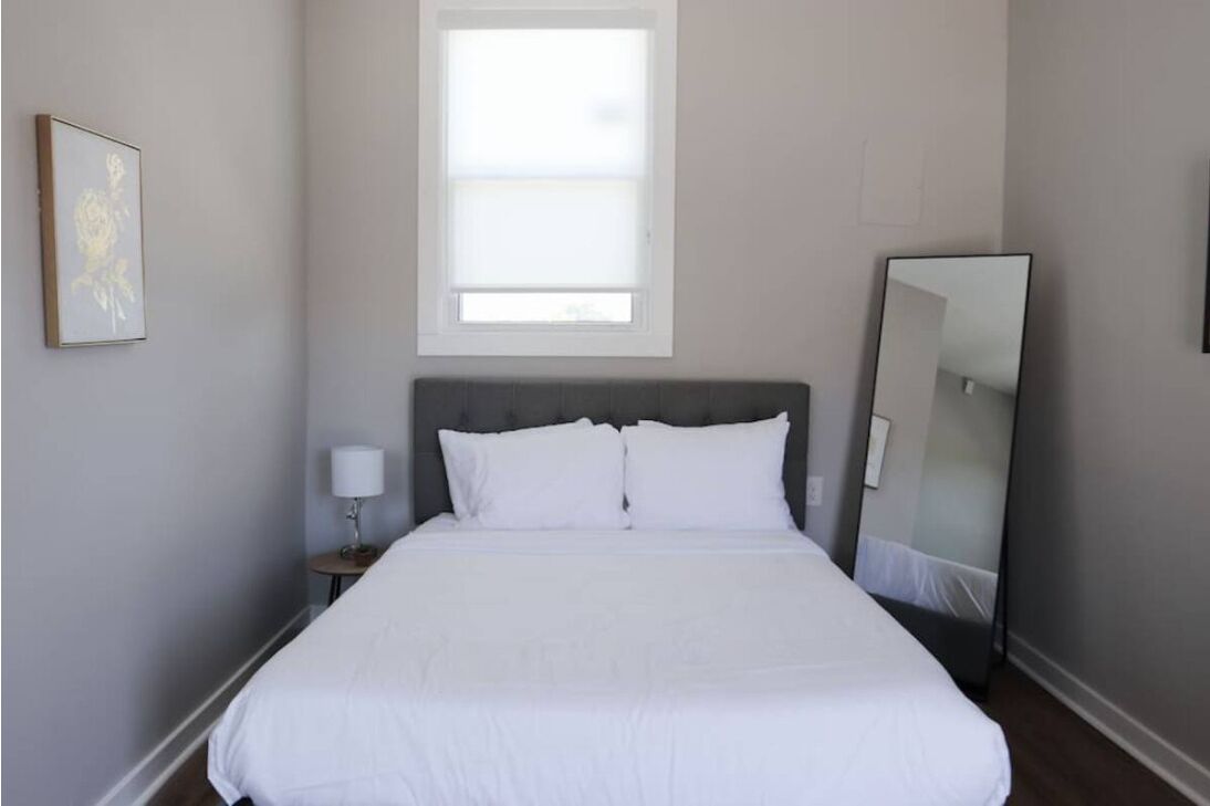Une chambre d’hôtel avec un grand lit, une table de chevet avec une lampe, une fenêtre et un miroir.